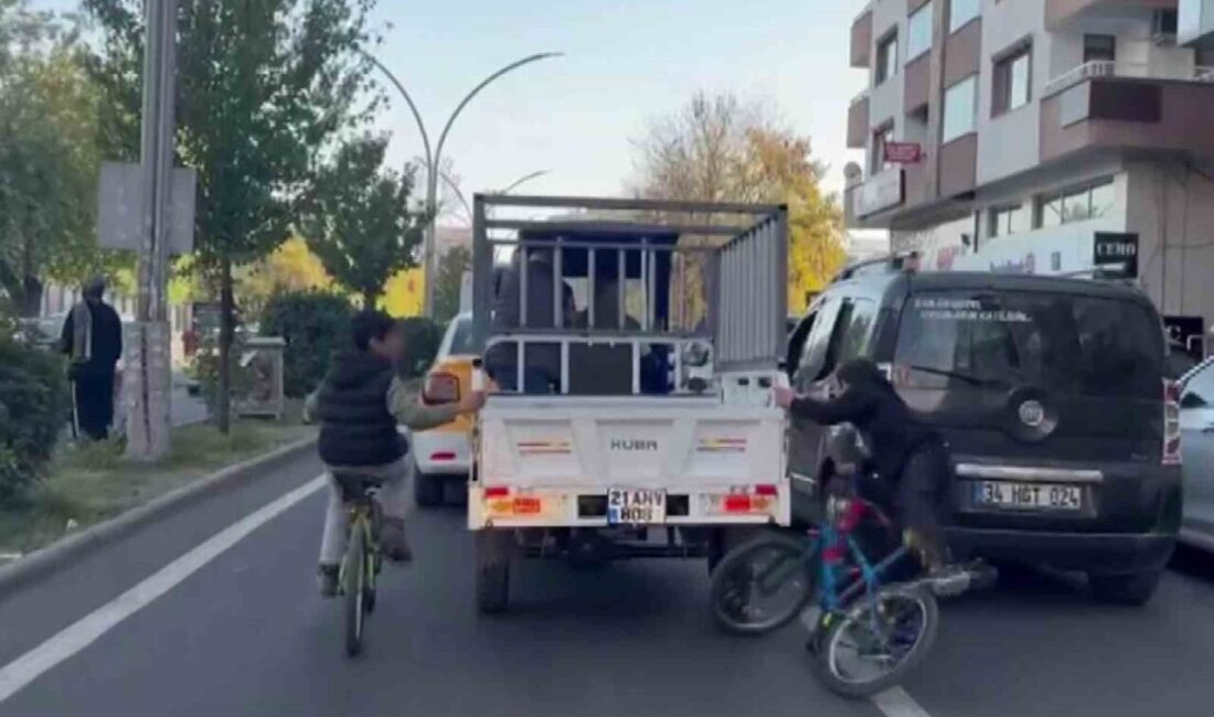 Diyarbakır’da Bisikletli Çocukların Sepetli Motosikletten Düşme Tehlikesi! Diyarbakır'ın Yenişehir ilçesinde, iki çocuk bisikletle sepetli bir motosiklete tutunarak